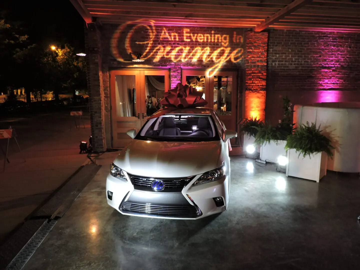 A sleek silver Lexus car is showcased indoors with warm orange lighting.