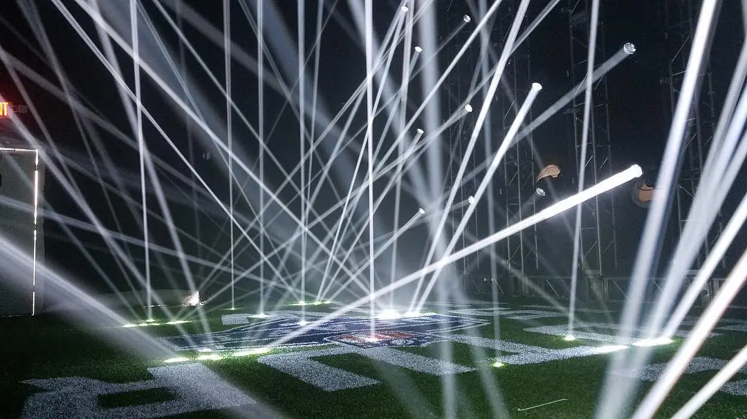 Bright white lights crisscross over a dark stage at night.
