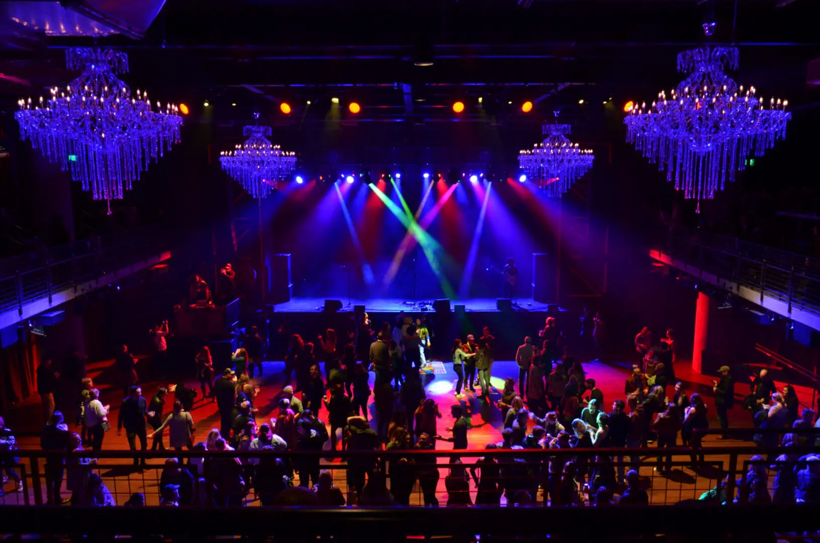 Colorful stage lights illuminate a lively concert crowd in a grand venue.