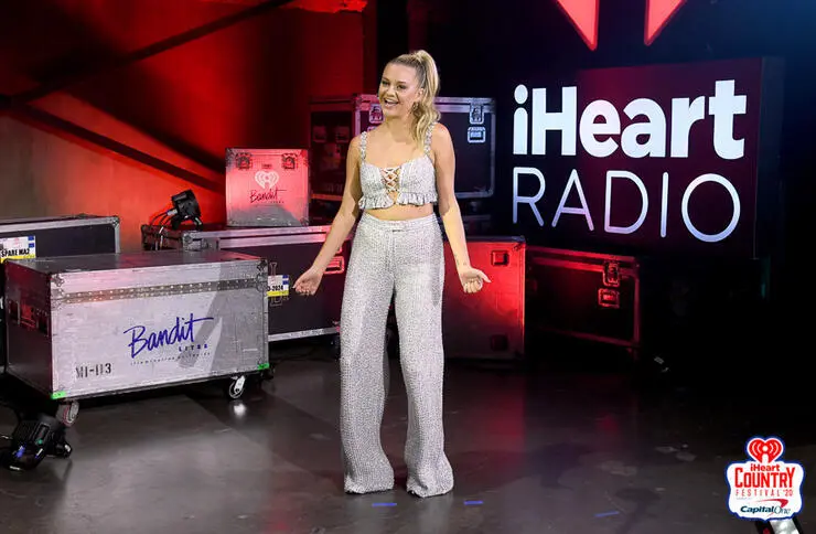 A woman in a sparkling outfit poses on an iHeartRadio stage.