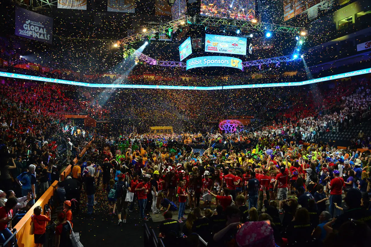A large crowd gathers in an arena with colorful flags and bright lights.