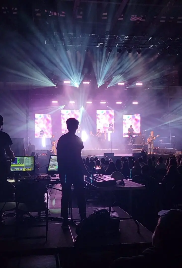 Silhouetted crew member overseeing a vibrant concert stage with bright lights.