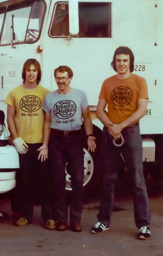 Three men wearing vintage graphic t-shirts standing together outdoors.