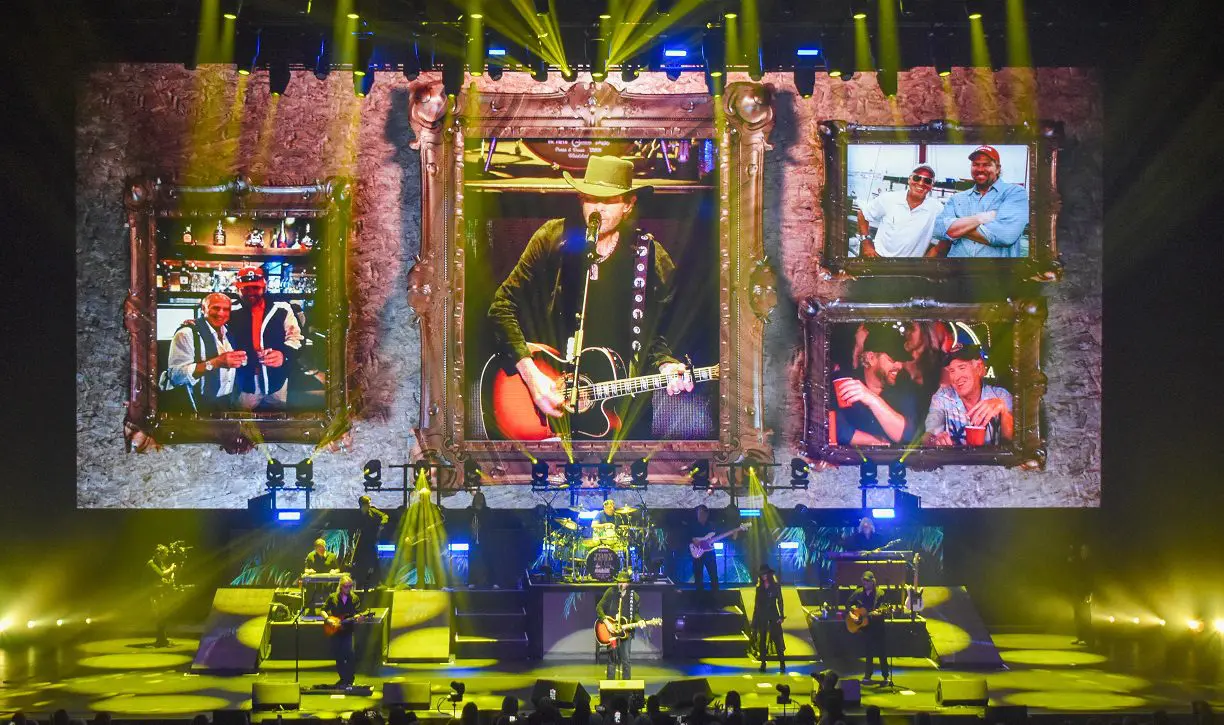 Concert stage with large framed video screens and vibrant lighting effects.