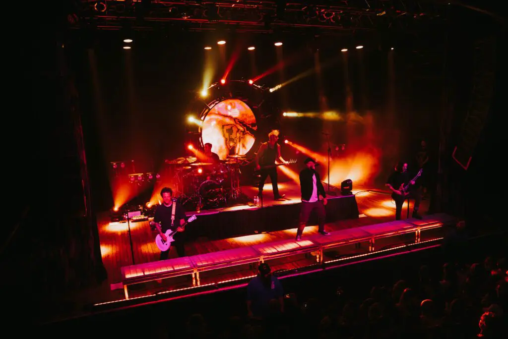 A band performs on stage with vibrant orange and red lighting effects.