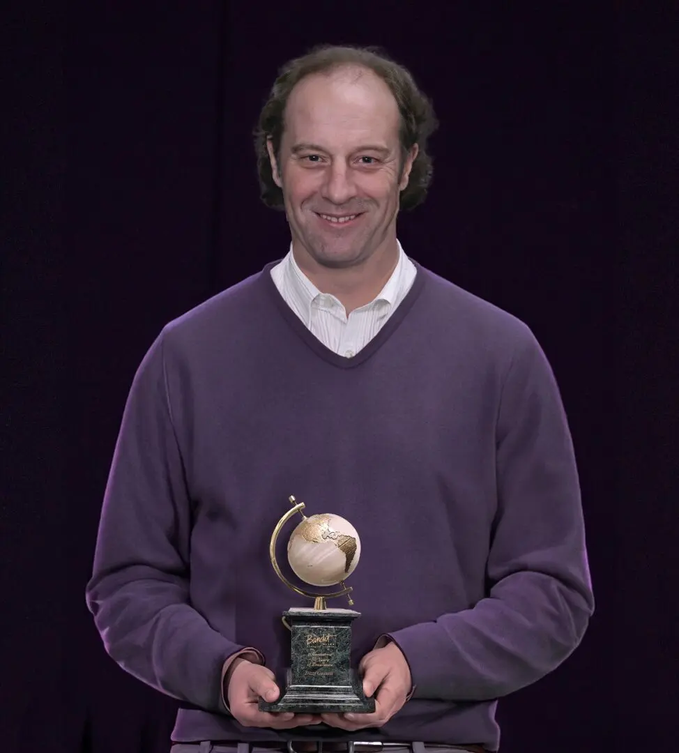 Man in purple sweater holding a baseball trophy and smiling.