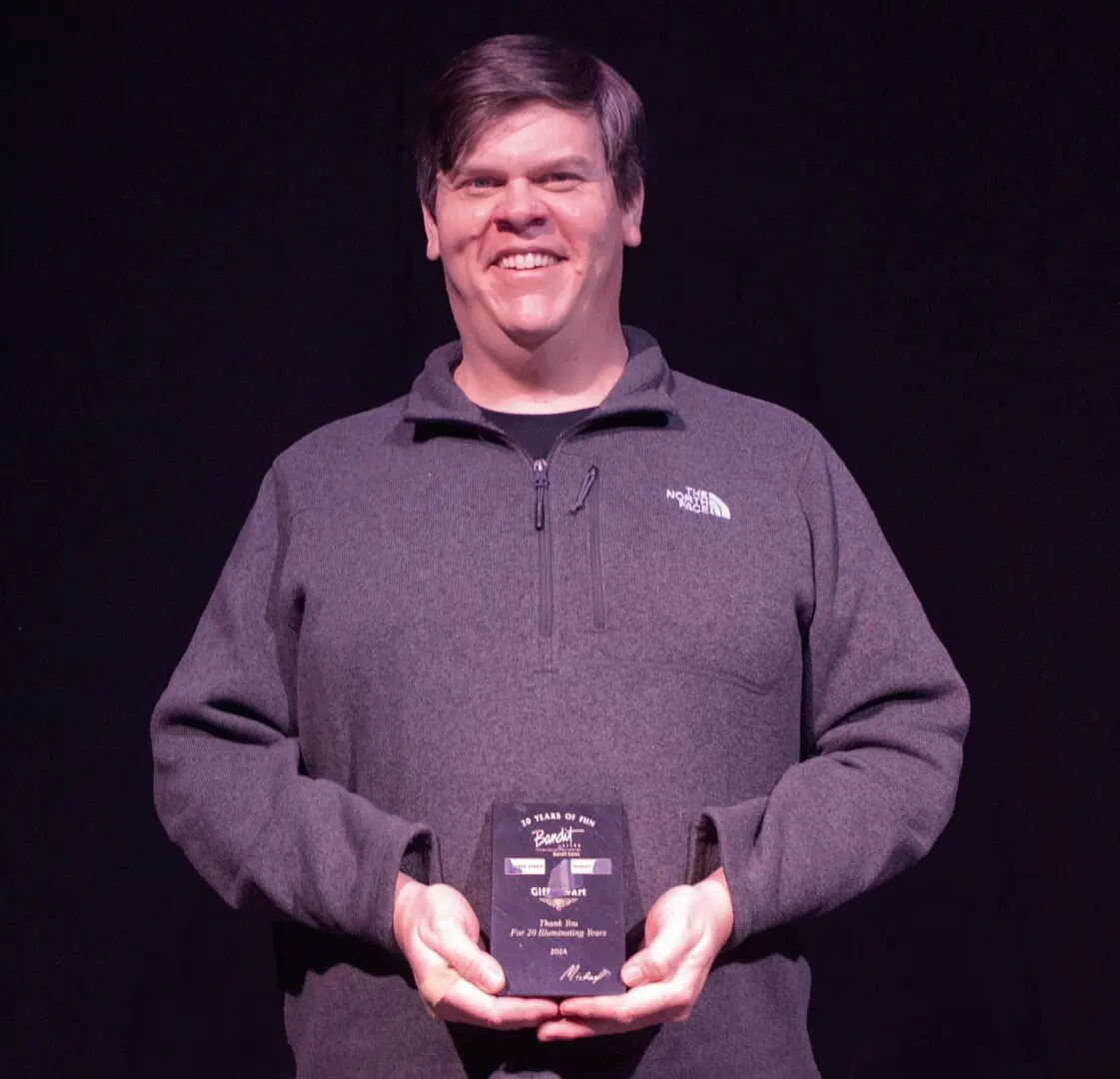 Man smiling and holding an award plaque on stage.