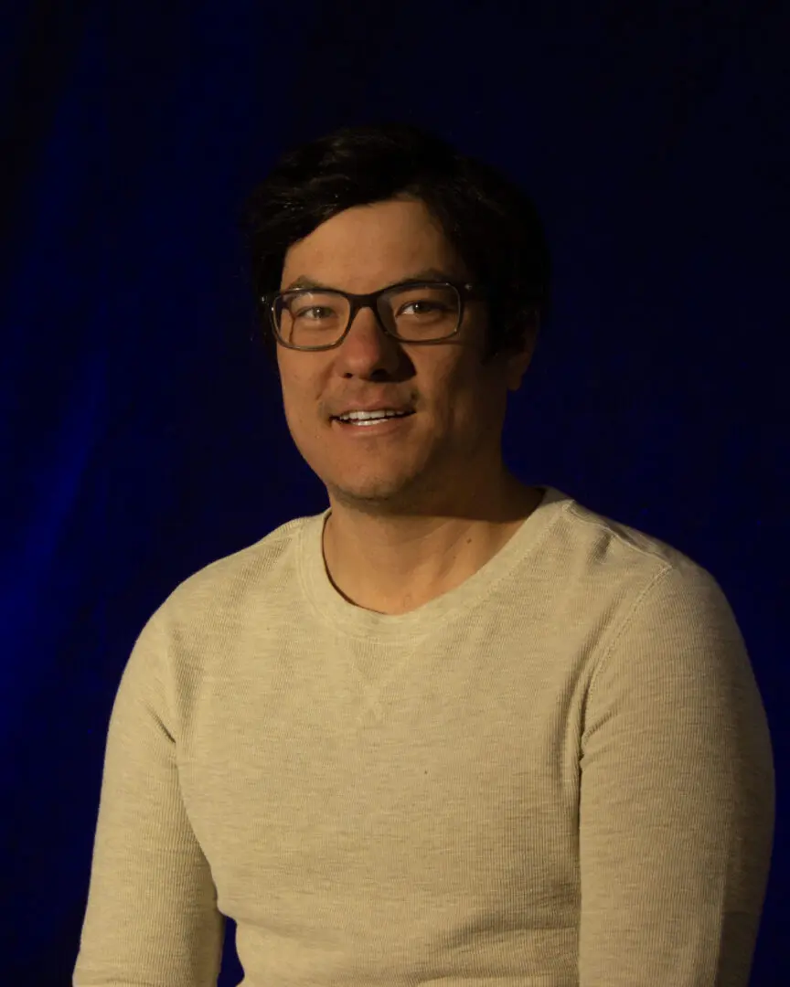 Man with glasses smiling against a dark background.