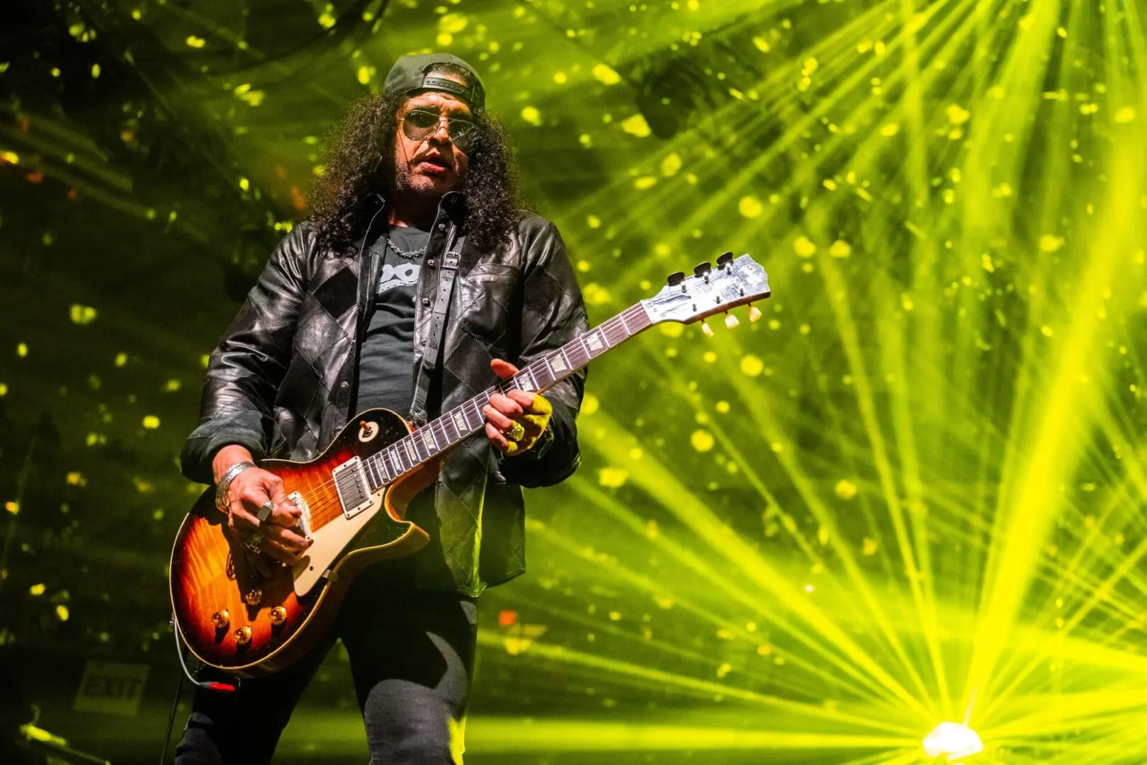 Guitarist performing energetically on stage with vibrant yellow lights.
