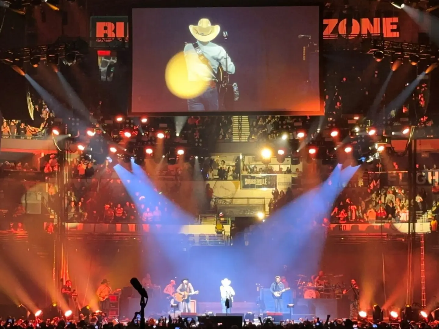 A lively concert with bright stage lights and a cowboy hat performer.