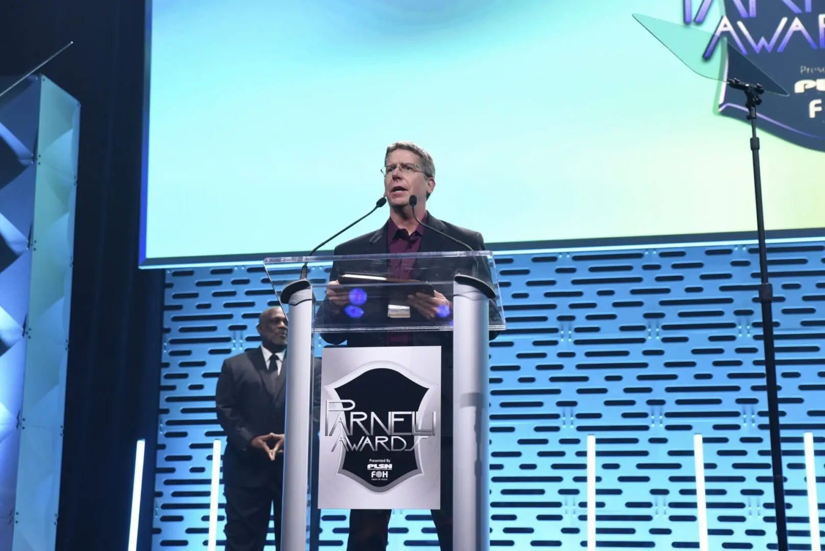 A man speaking at a podium with a microphone on stage.