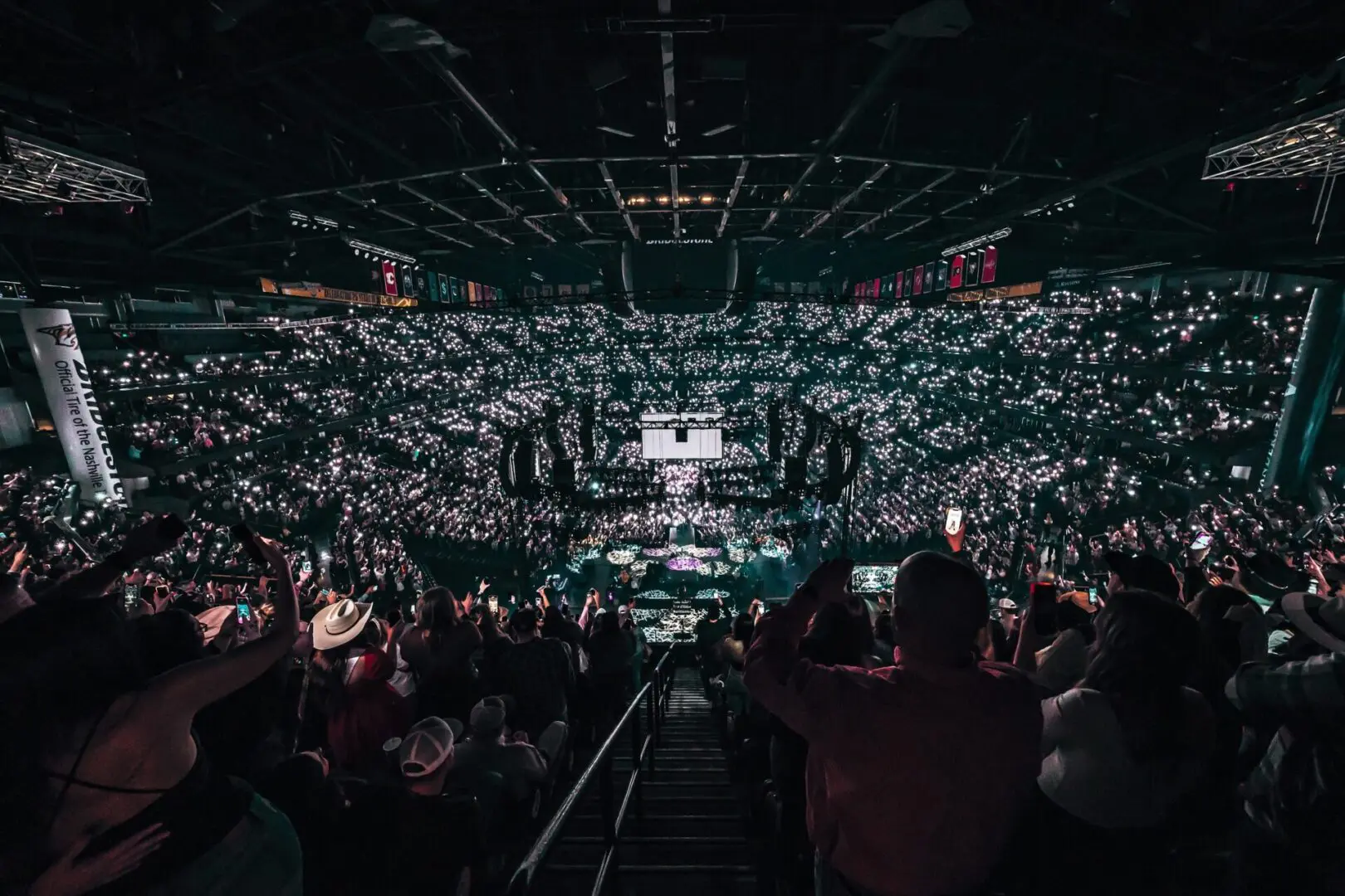 A packed indoor arena with an enthusiastic crowd holding up lights.