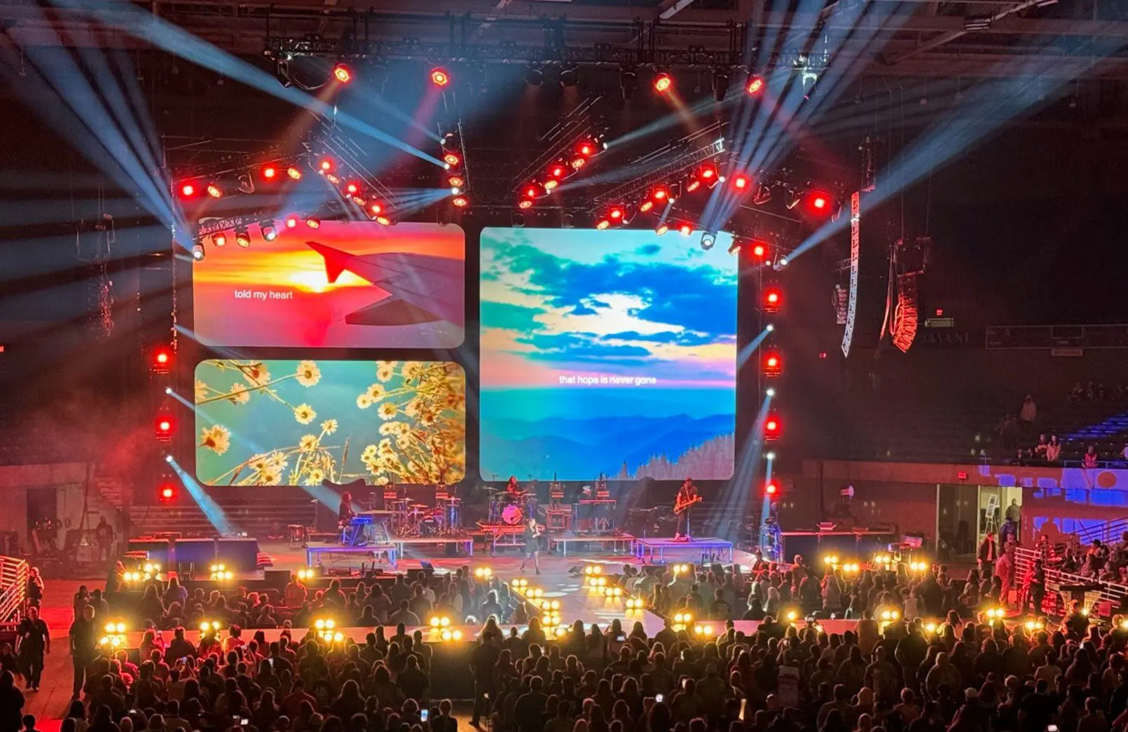 A vibrant concert stage with bright lights and large screens displays colorful visuals.