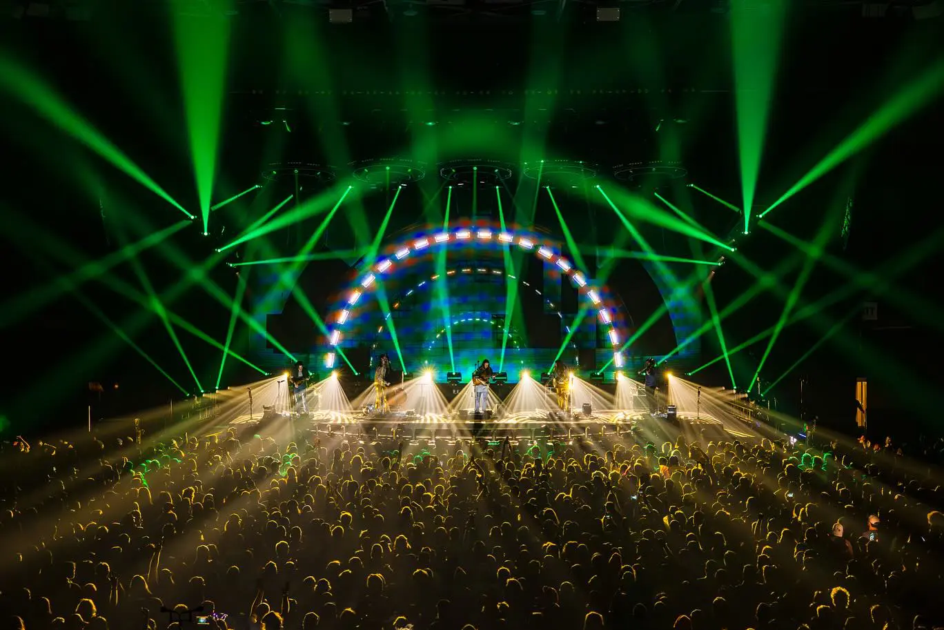 A vibrant concert scene with green laser lights and a large crowd.