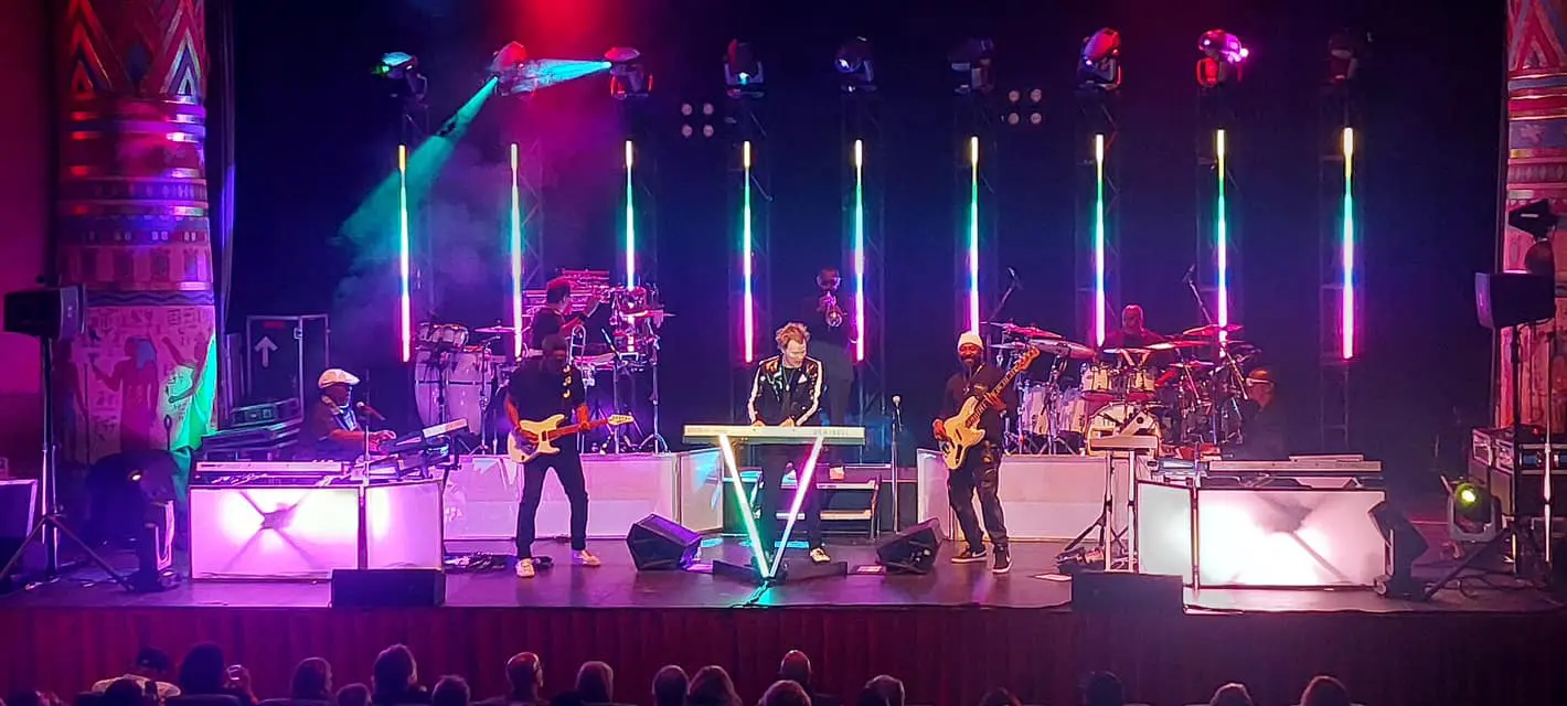 A vibrant live band performs on stage with colorful vertical lights.