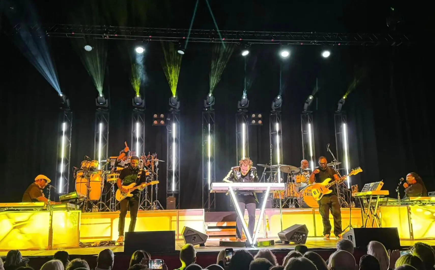 A lively band performs on stage with vibrant lighting and energetic musicians.