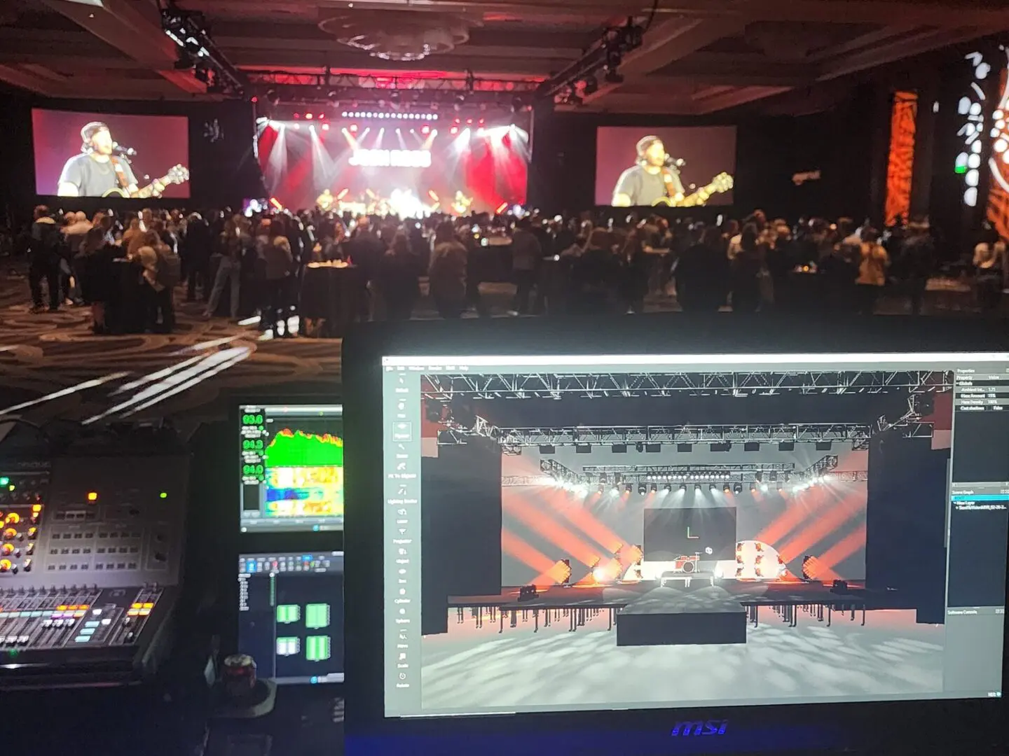 A live band performs on stage with bright spotlights and a crowd watching.