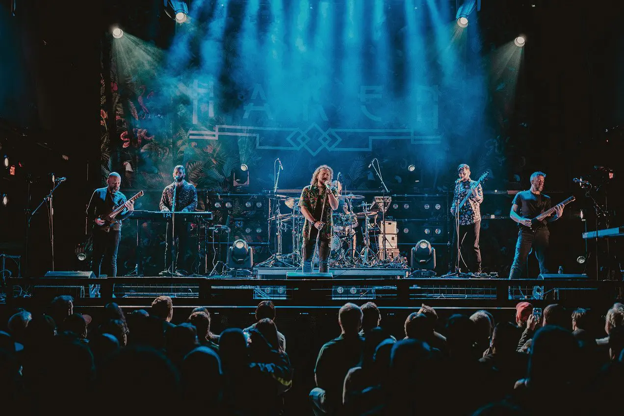 A band performs energetically on stage with blue lighting and an engaged audience.