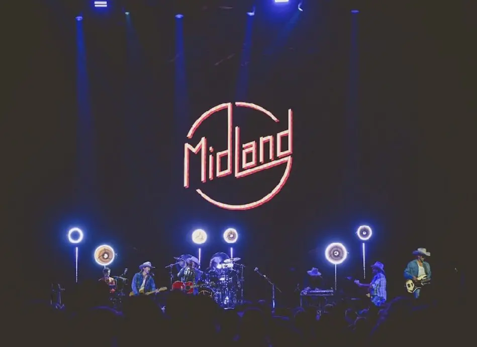 Midland band performing live on stage with bright circular lights.