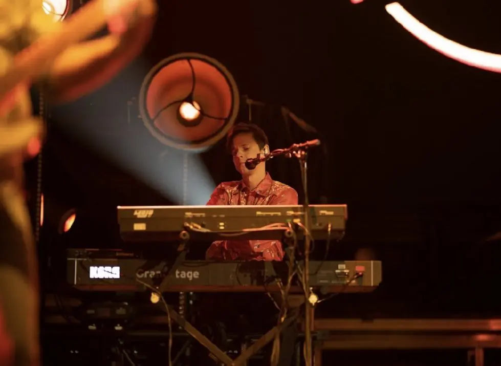 Musician playing keyboard on stage under spotlight.