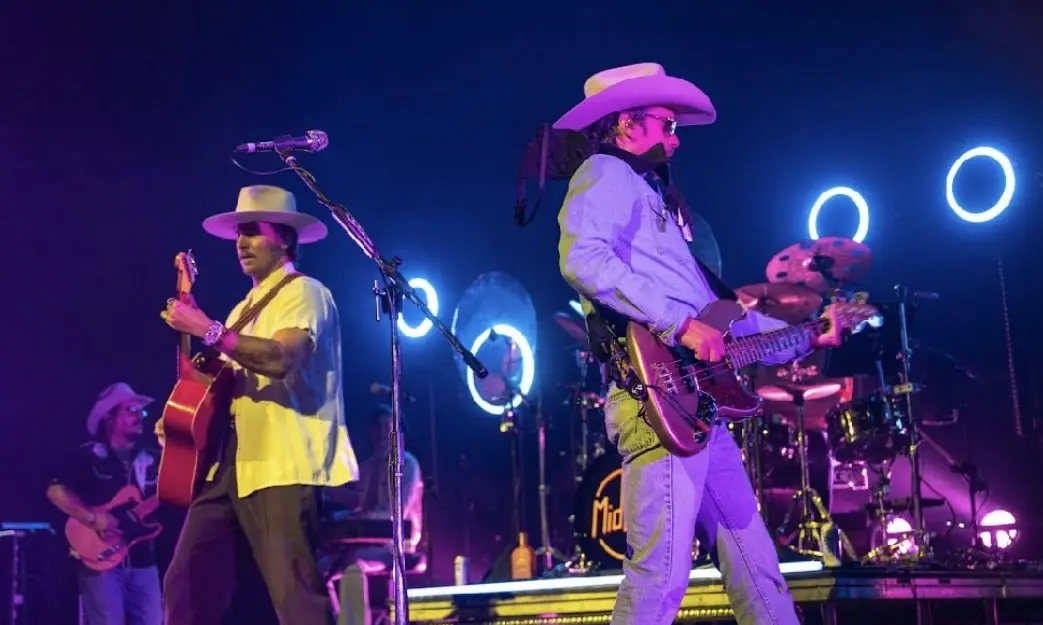 Two musicians perform on stage with colorful lights behind them.