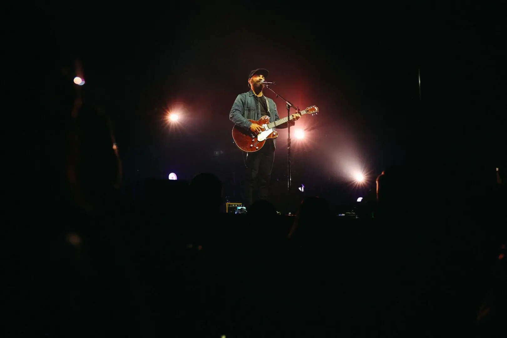 Musician playing guitar on stage with dramatic lighting.