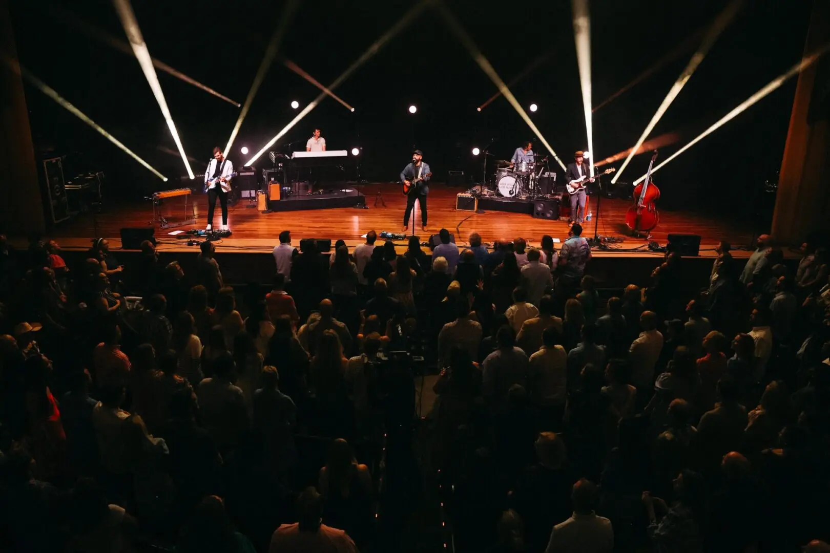 A band performing live on stage with lights and a large audience.