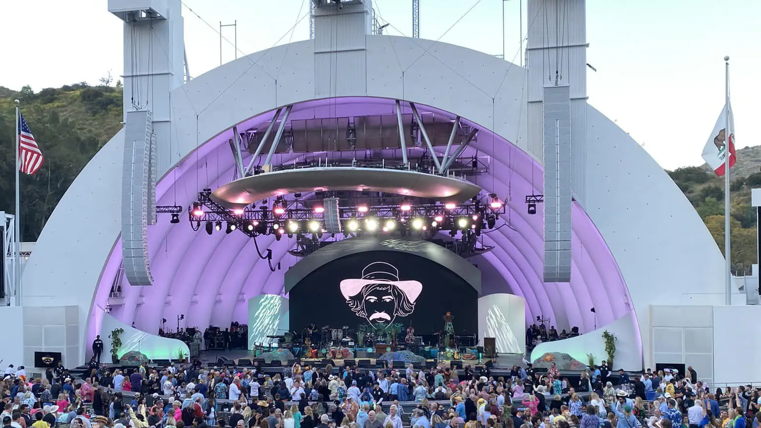 Outdoor concert with a large crowd at a purple-lit band shell.
