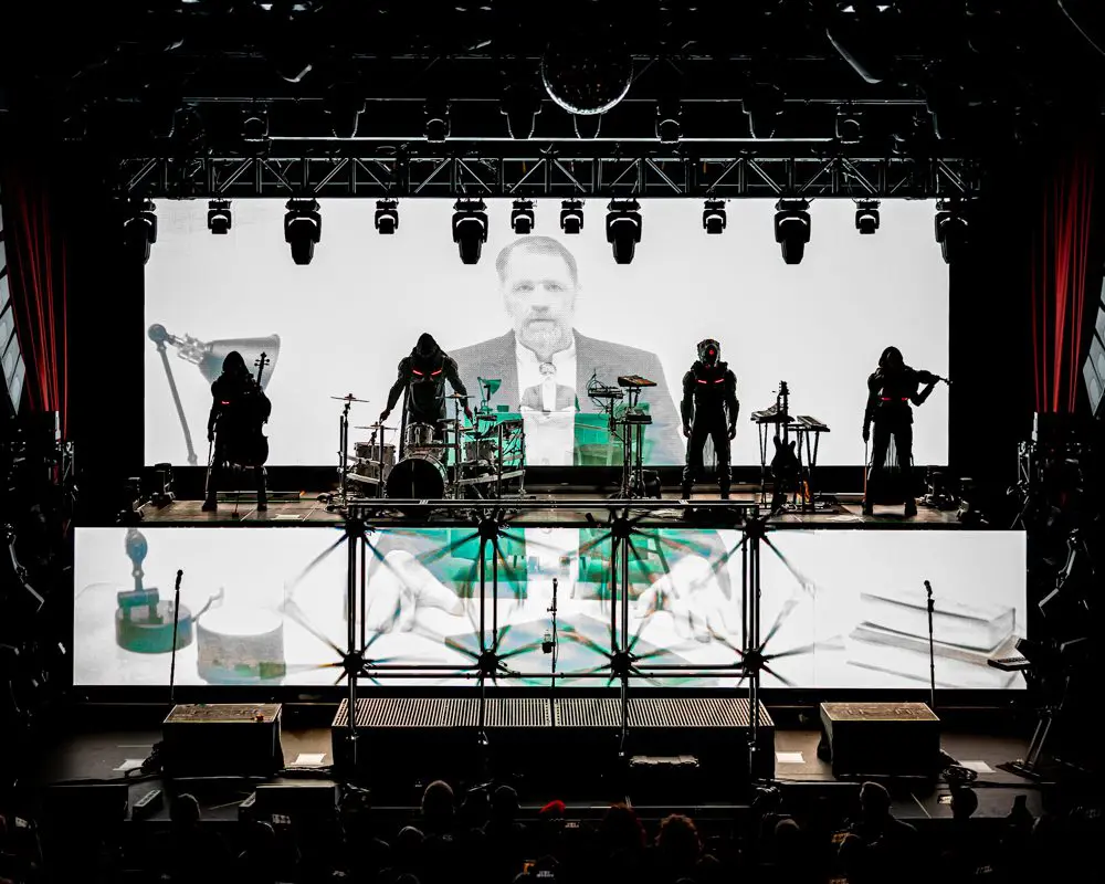 Silhouetted band performing with a large black-and-white video projection behind them.