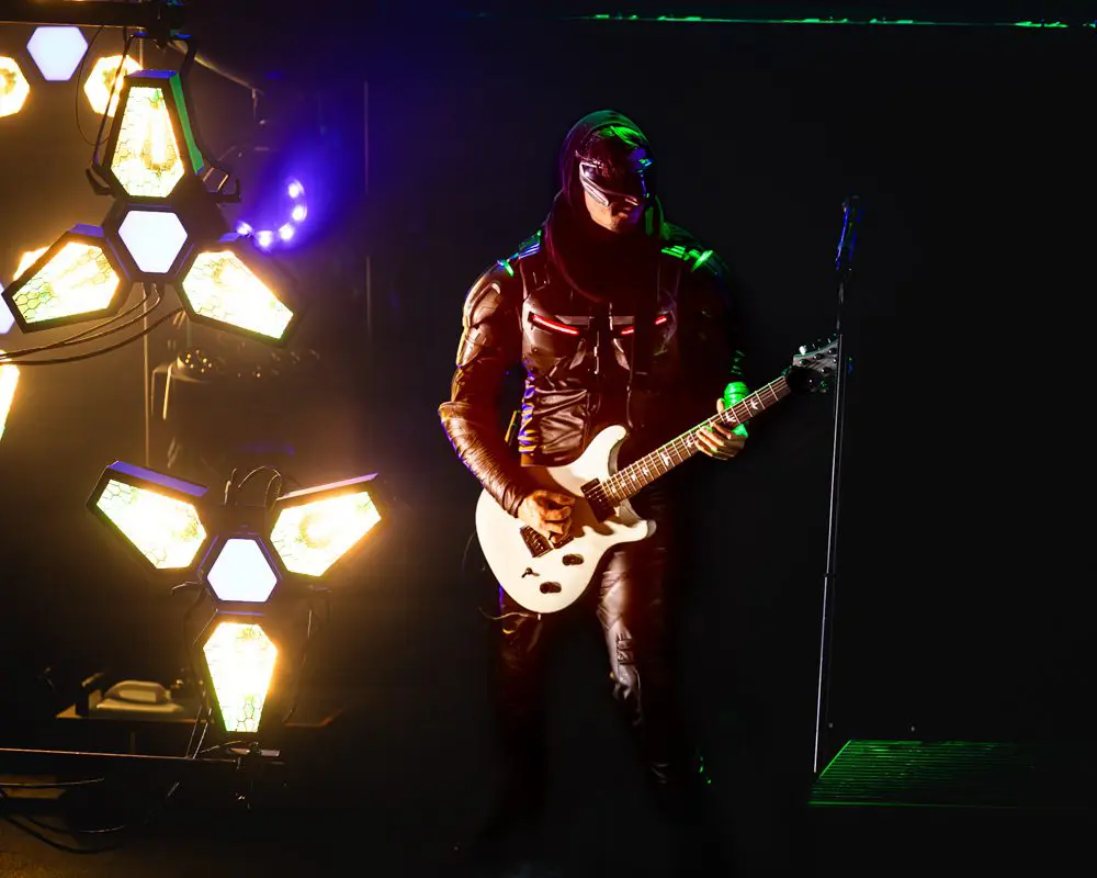 Guitarist performing on stage with vibrant lighting effects.