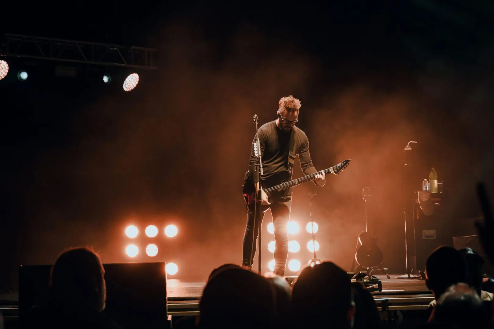 Guitarist performing on stage with bright lights behind.