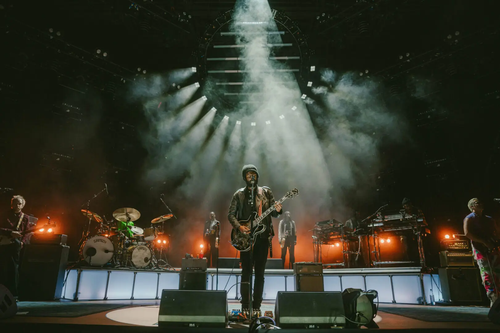 Musician playing guitar on a dimly lit stage with dramatic smoke effects.