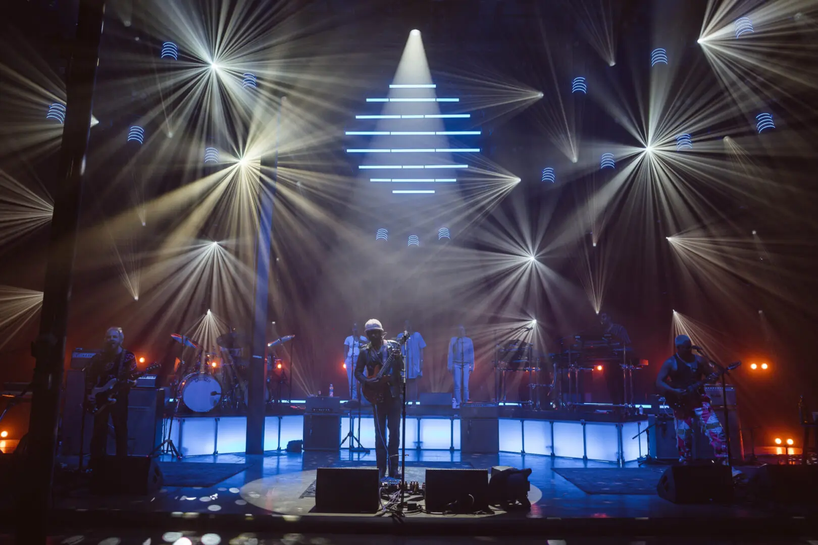A band performs under blue lights and a pyramid-shaped spotlight.