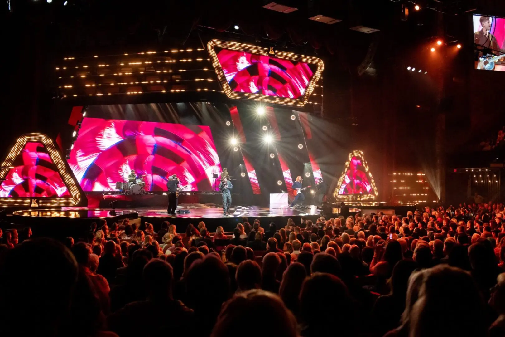 A lively concert with vibrant screens and a large crowd at night.