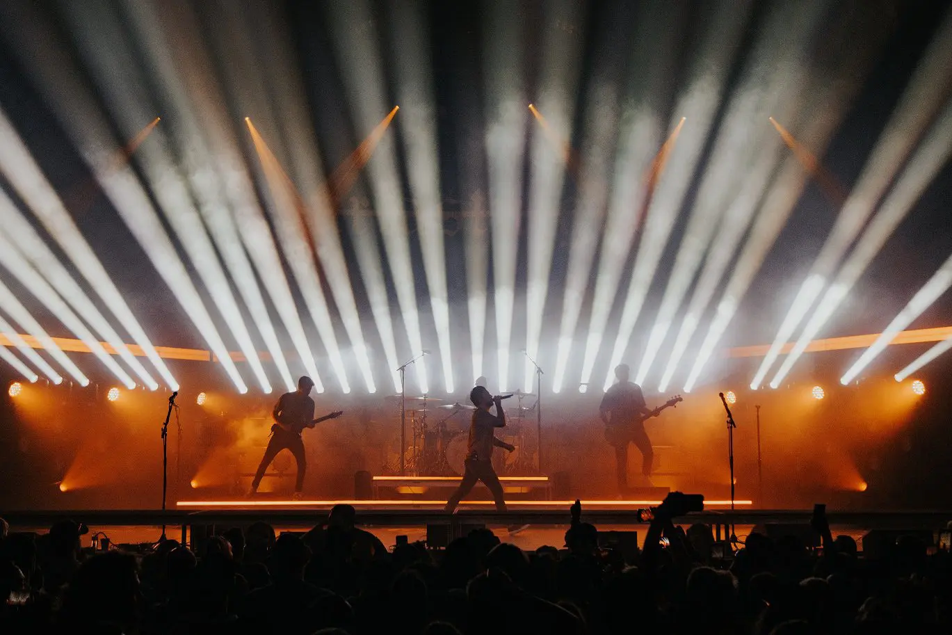 Rock band performing on stage with dramatic lighting and fog effects.