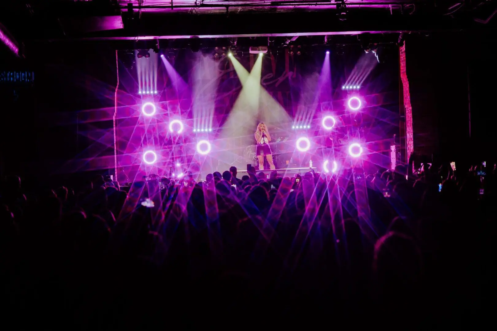Concert stage with vibrant purple lighting and enthusiastic crowd.
