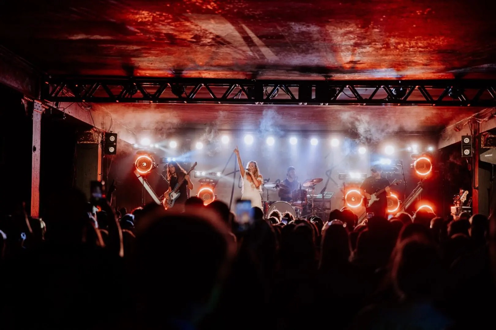 A vibrant concert scene with a band performing under red and white lights.
