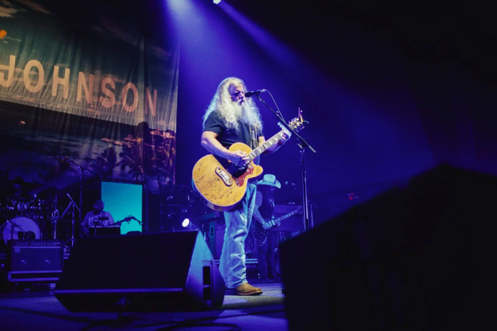 Musician performing live on stage with guitar under blue lighting.