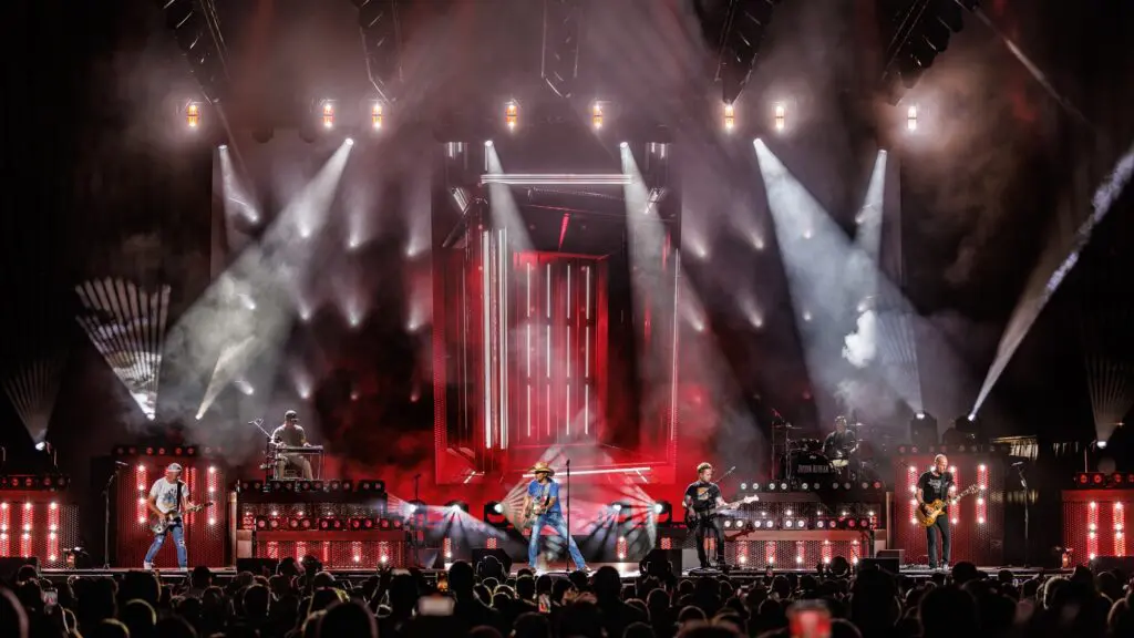 A rock band performs on a brightly lit stage with red and white lights.