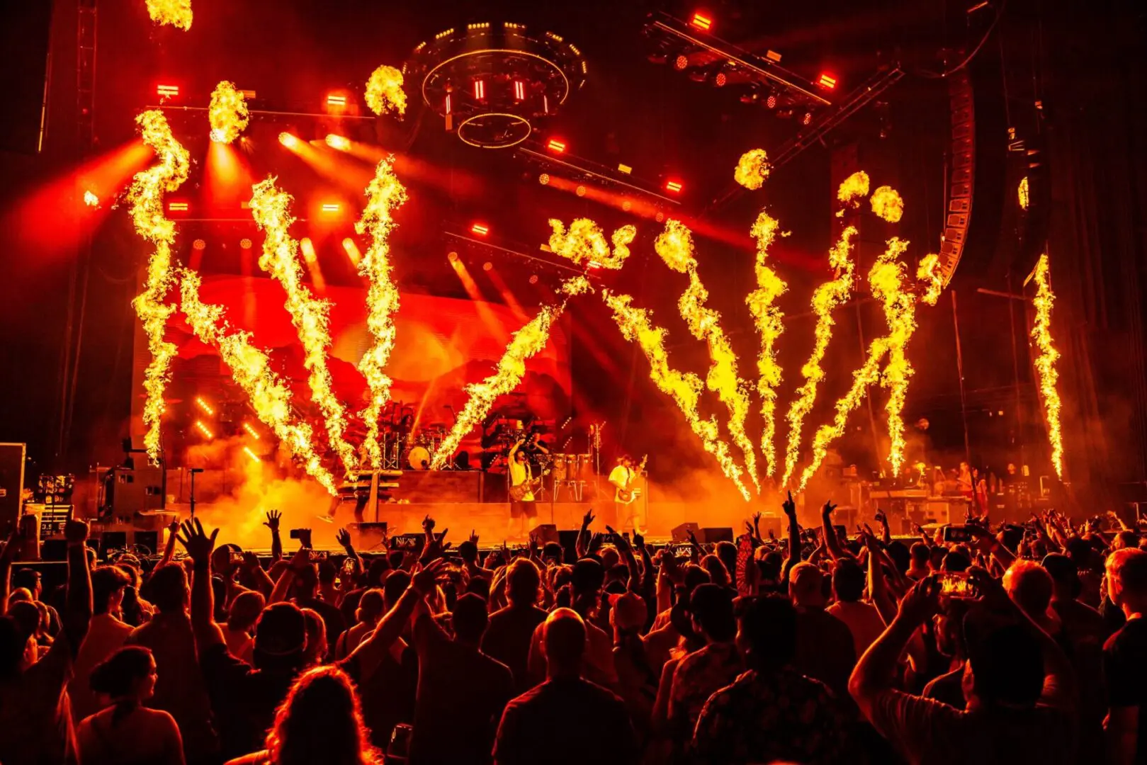 Crowd enjoying a fiery concert with pyrotechnics and bright lights.