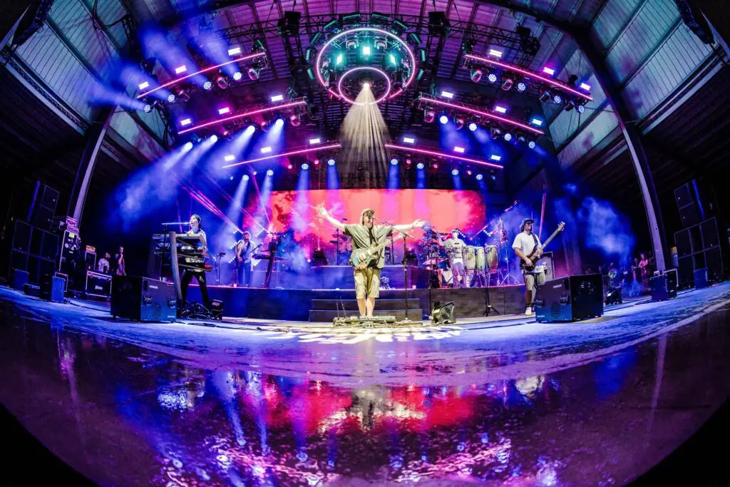 A vibrant band performs on a colorful, illuminated stage with dynamic lighting effects.