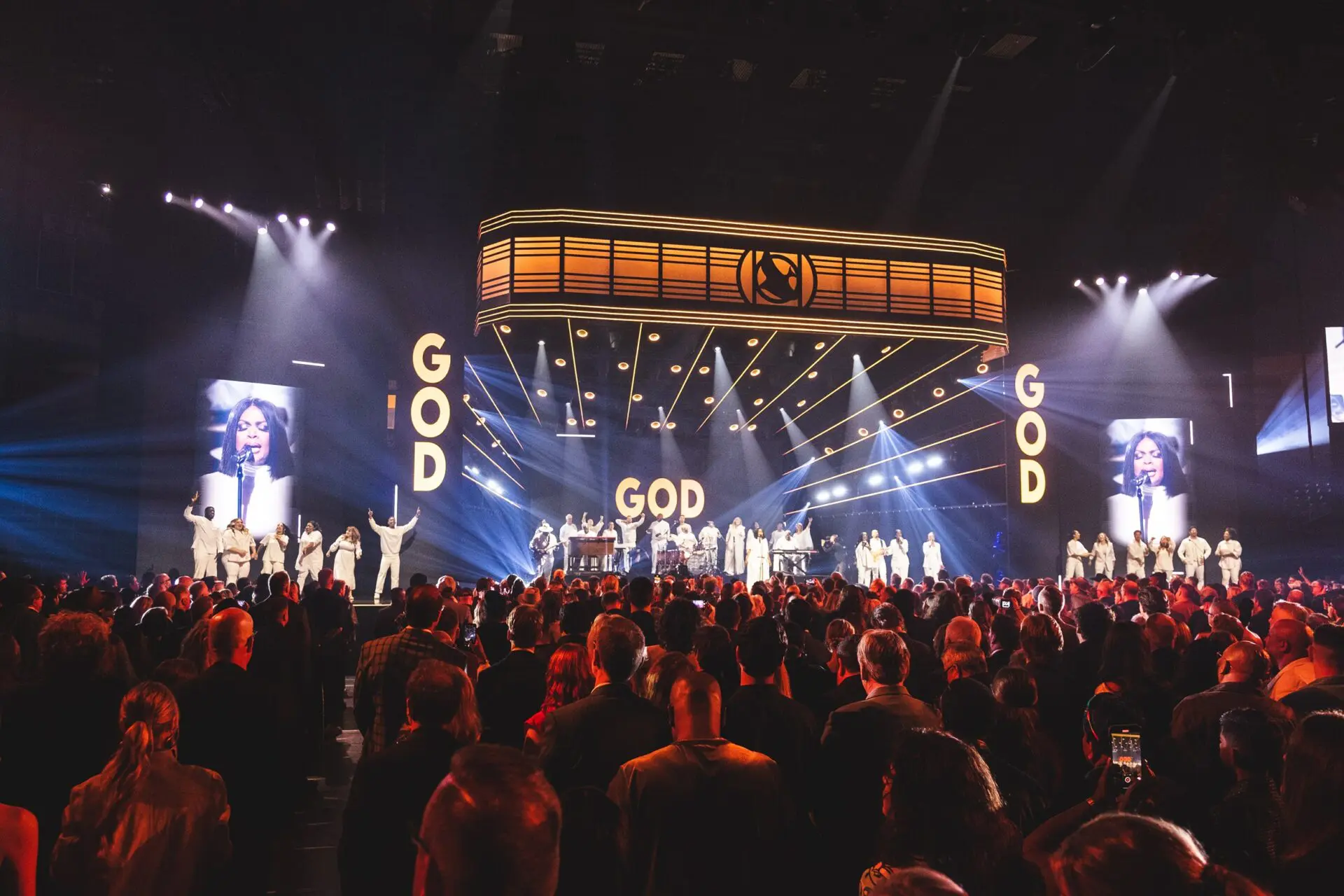 A large crowd at a concert with 'GOD' displayed prominently on screens.