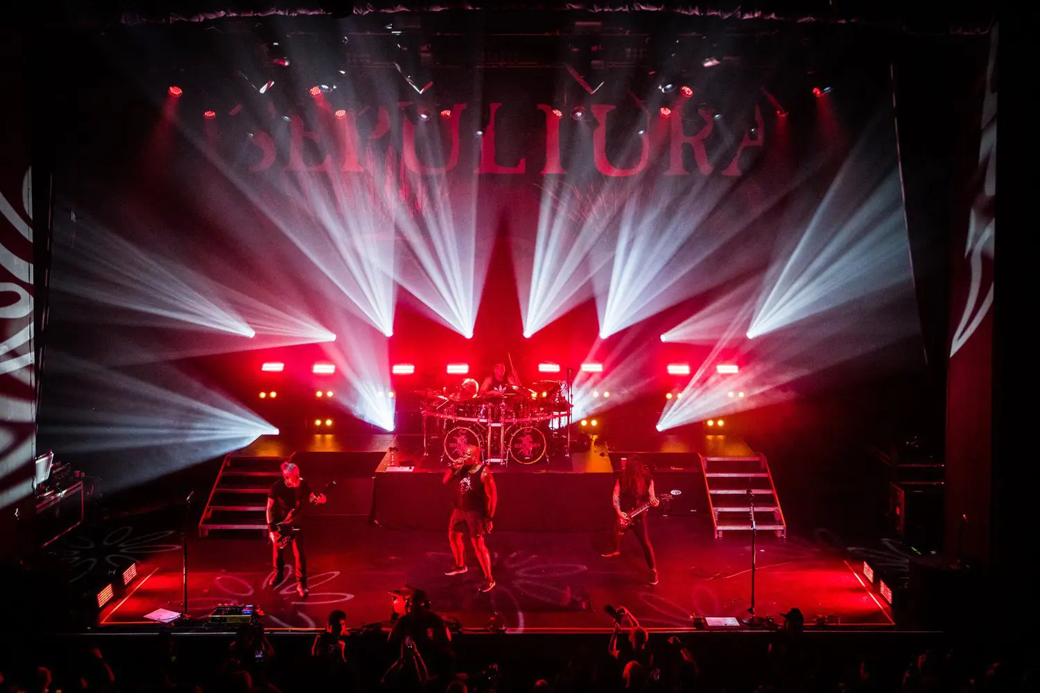 Rock band performing live on stage with dramatic red and white lighting.
