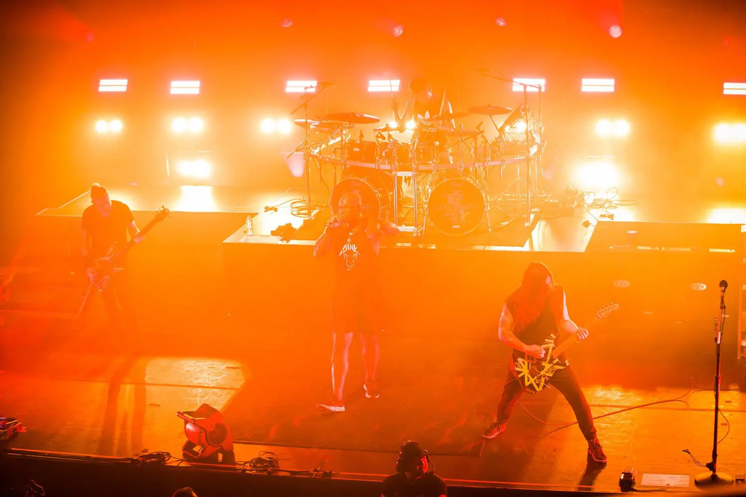 A band performs energetically on stage with bright orange lights.