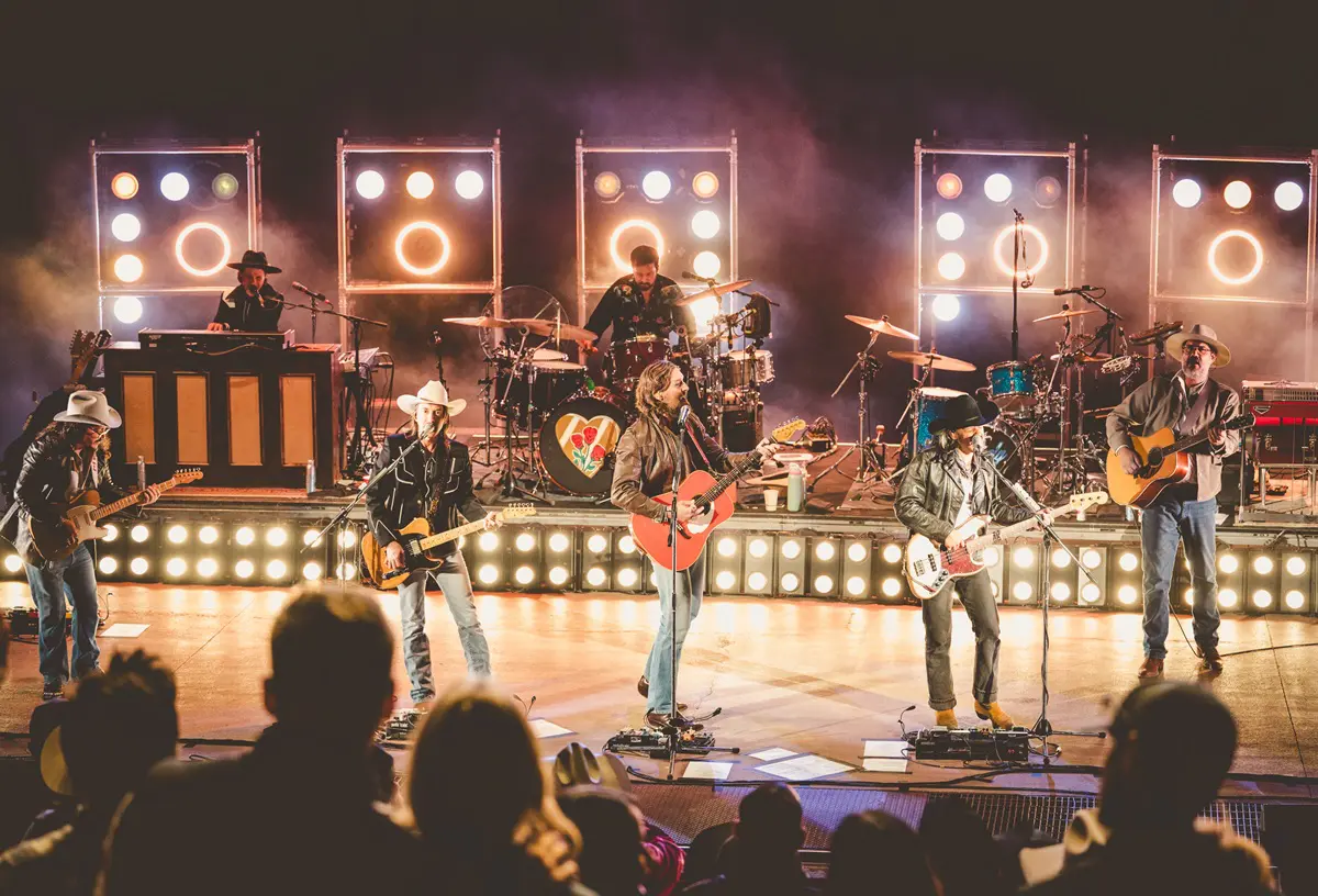 A band performs energetically on stage with illuminated lights.