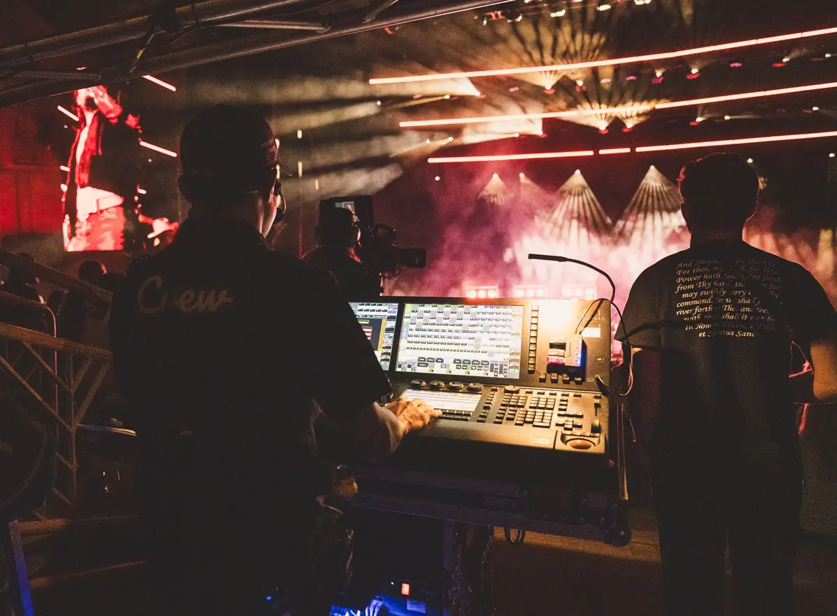 Two people operating a DJ mixing console in a dimly lit club.