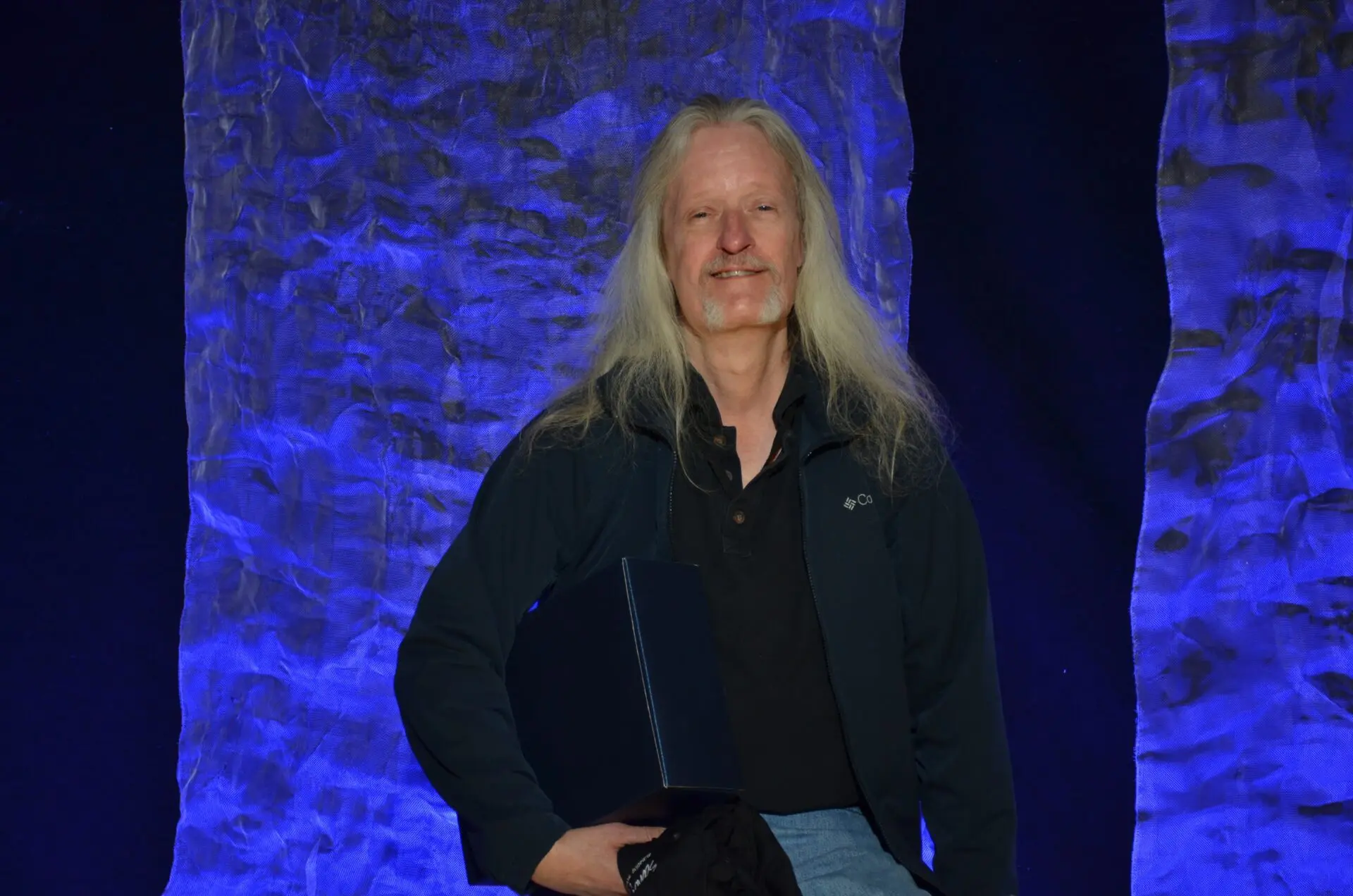 Man in a leather jacket and cap holding an award on stage.