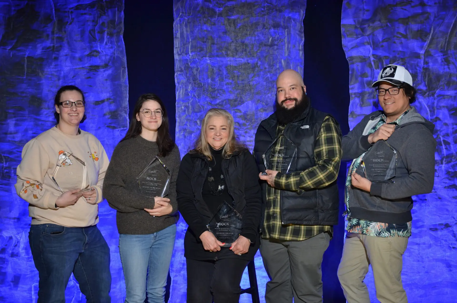 Five people posing together against a stone wall with blue lighting.