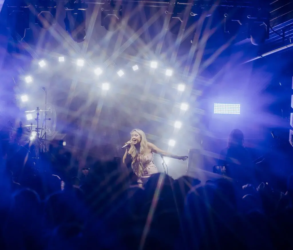 Singer performing on stage under bright lights with a lively crowd.