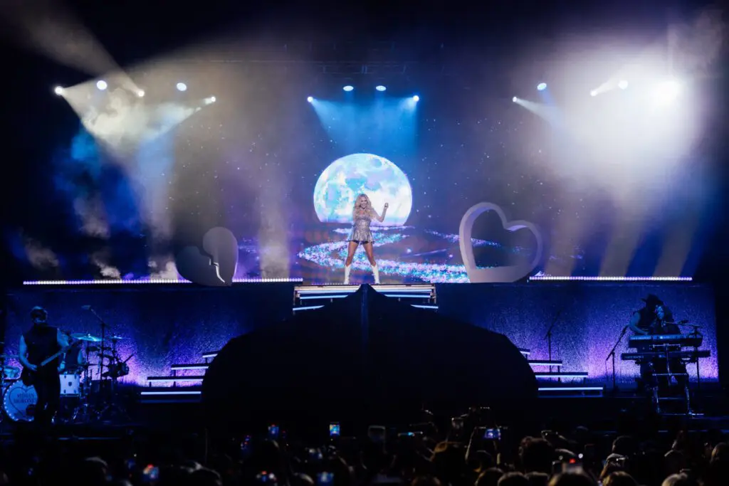 A singer performs on a large stage with dramatic lighting and a moon backdrop.